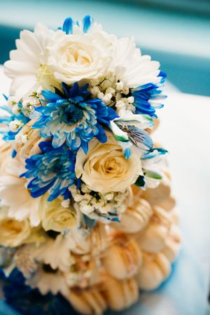 Beautiful wedding bouquet featuring cream roses and bright blue flowers against a turquoise background.