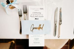 Elegant Baby shower menu card with gold lettering displayed with silver cutlery on white tablecloth.
