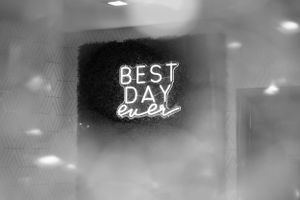 A neon sign reading 'BEST DAY EVER' glows in black and white against a dreamy background.