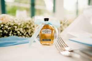 Miniature maple syrup bottle baby shower favor with blue ribbon placed by silverware.