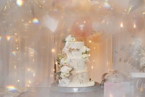 An elegant white wedding cake decorated with fresh flowers sits beneath twinkling lights.