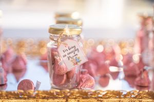 Mason jars filled with pink candies and gold accents displayed on a reflective surface with soft bokeh lighting.