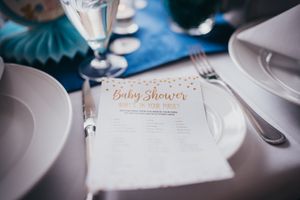 Baby shower invitation card placed on an elegant table setting with white plates and silverware against a blue background in the Hudson Vall