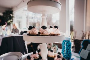 Pink frosted cupcakes displayed on a white tiered cake stand with black garnishes.