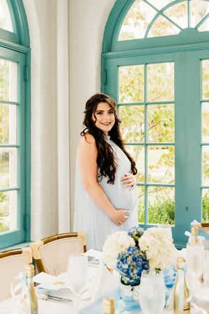Elegant maternity photo by turquoise-framed windows in baby shower reception setting in the Hudson Valley,NY.
