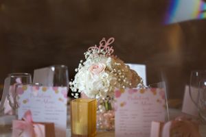 Elegant wedding reception centerpiece with white flowers and baby's breath in a gold vase next to place cards.