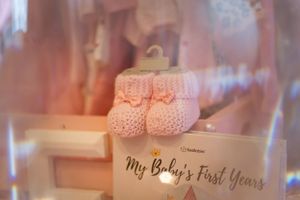 Pink baby booties displayed next to a 'My Baby's First Years' memory book.