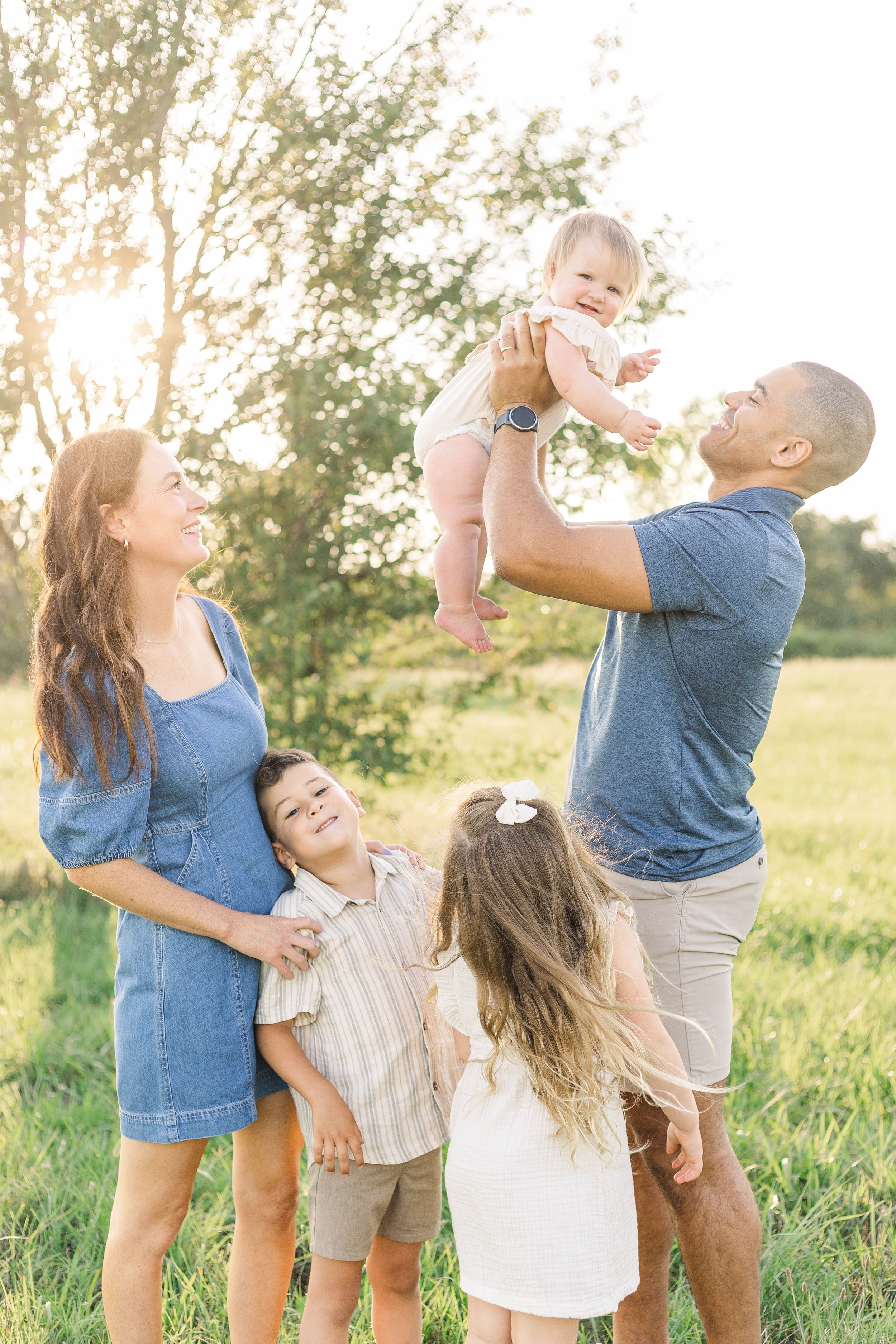 Father lifting his young child into the air while family watches during a playful outdoor family photography session.