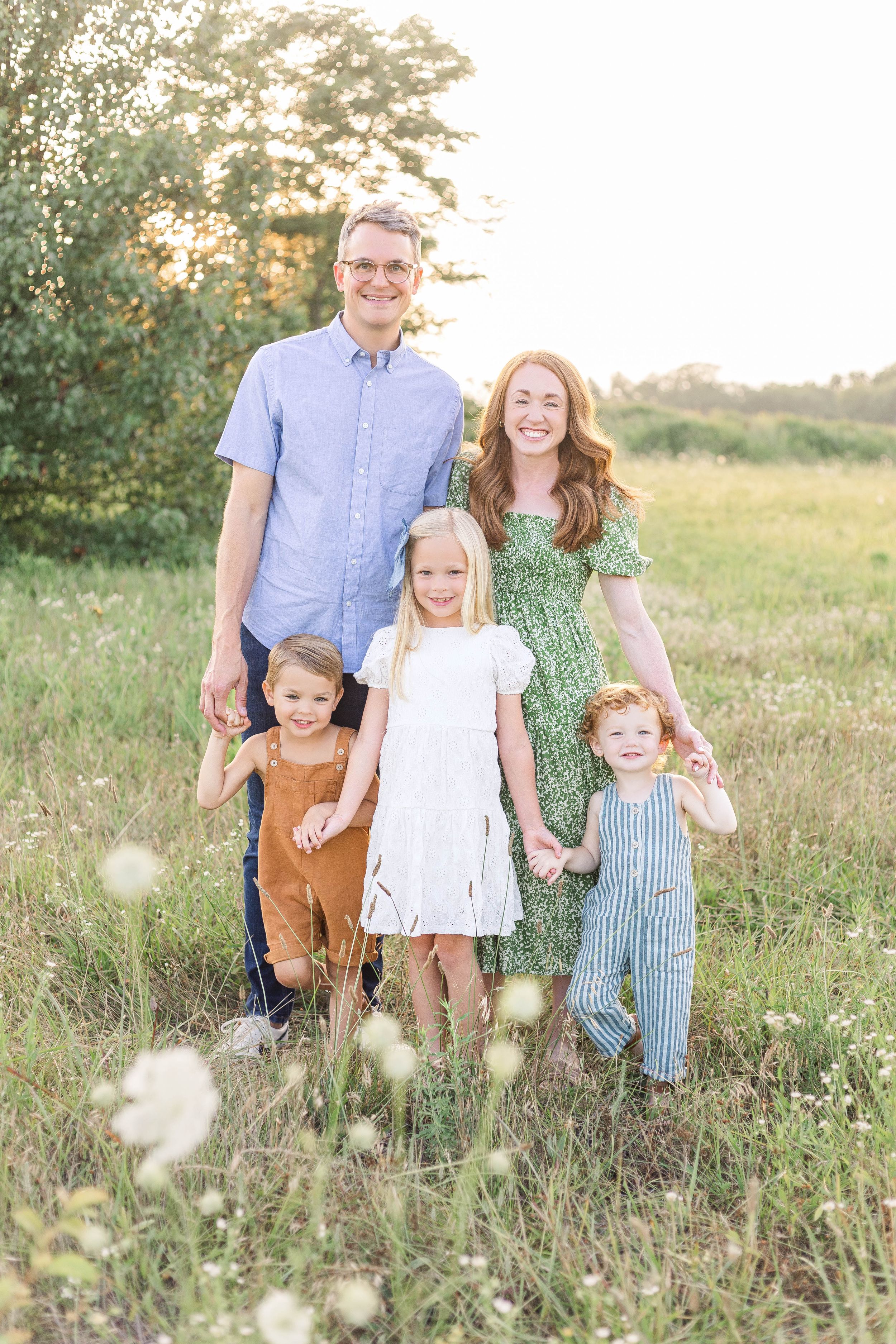Family of five standing together in a sunlit grassy field during an outdoor family portrait session.