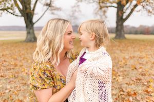 Mother and young daughter smiling at each other among golden autumn leaves during a candid fall family portrait session.
