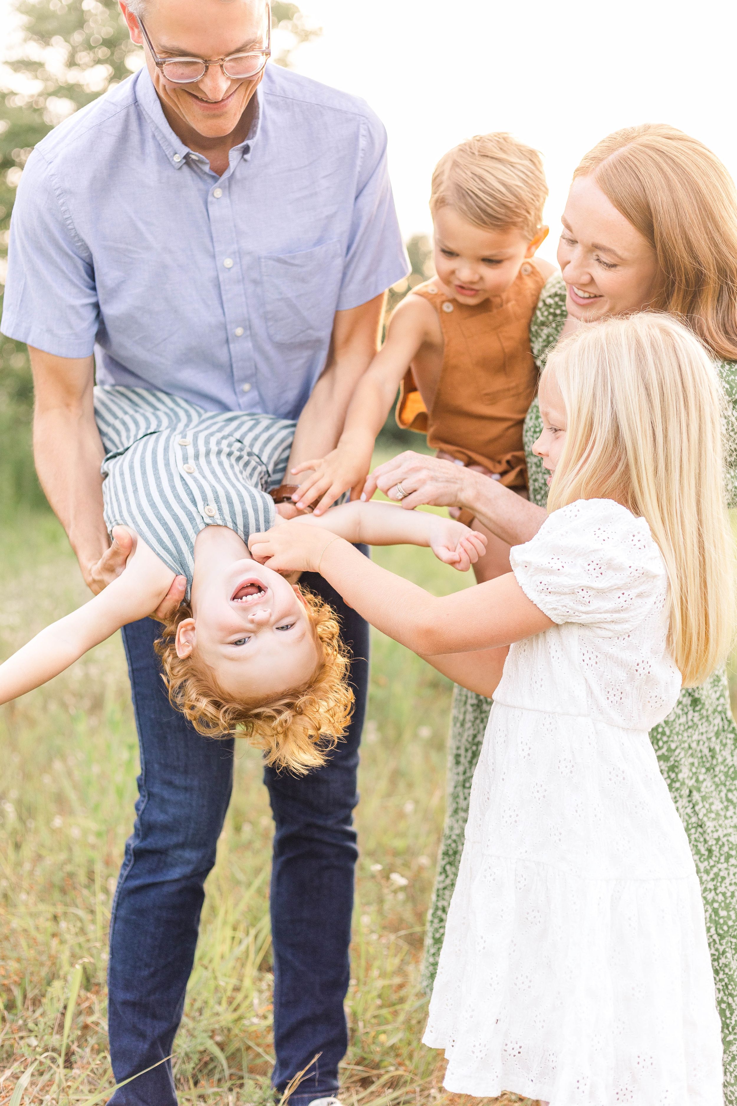 Parents and children laughing and playing together in a grassy field during a candid outdoor family photography session.