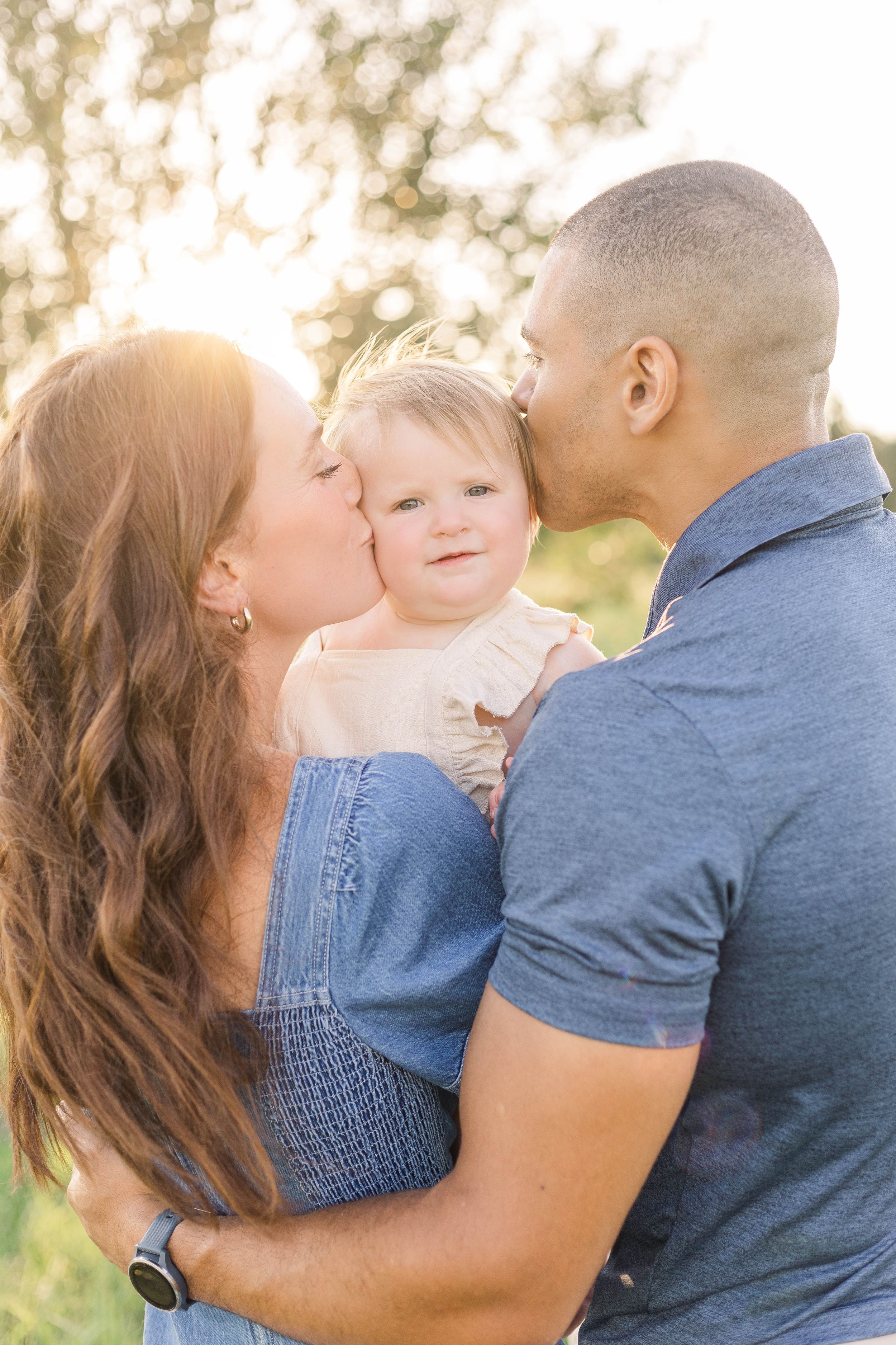 Mother and father smiling at their baby while holding them close during a warm, natural light outdoor family photography session.