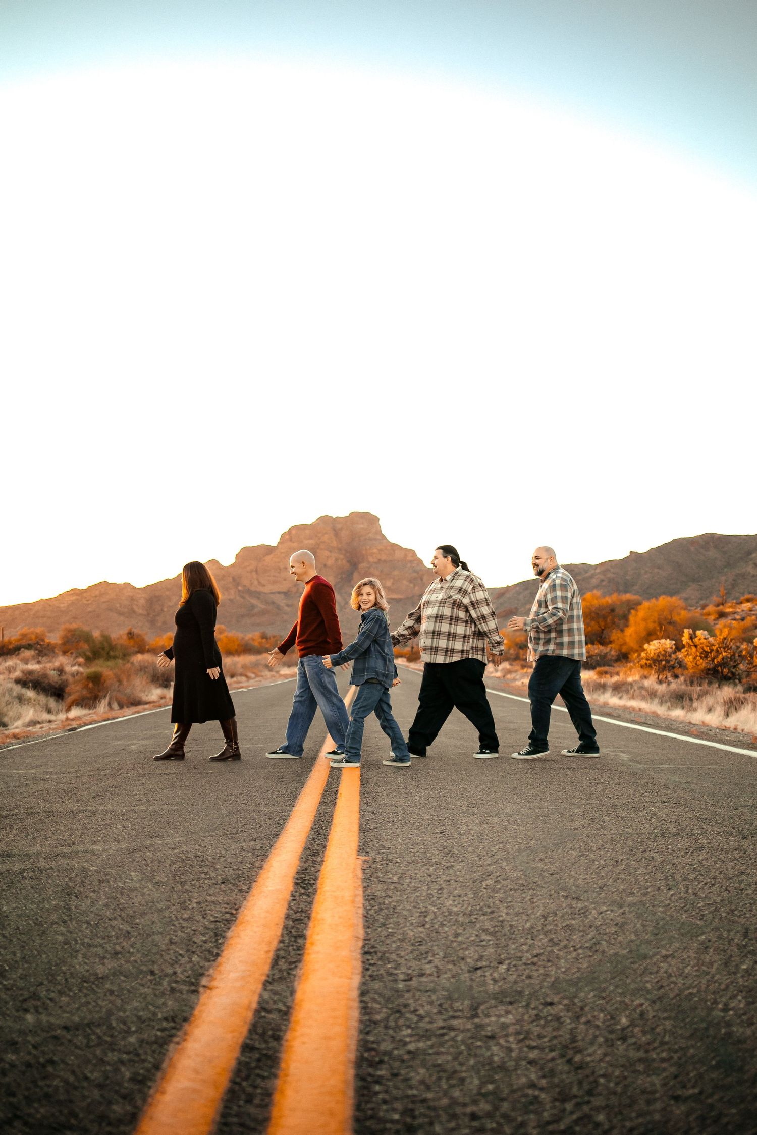 Group walking down the middle of a desert highway during golden hour.