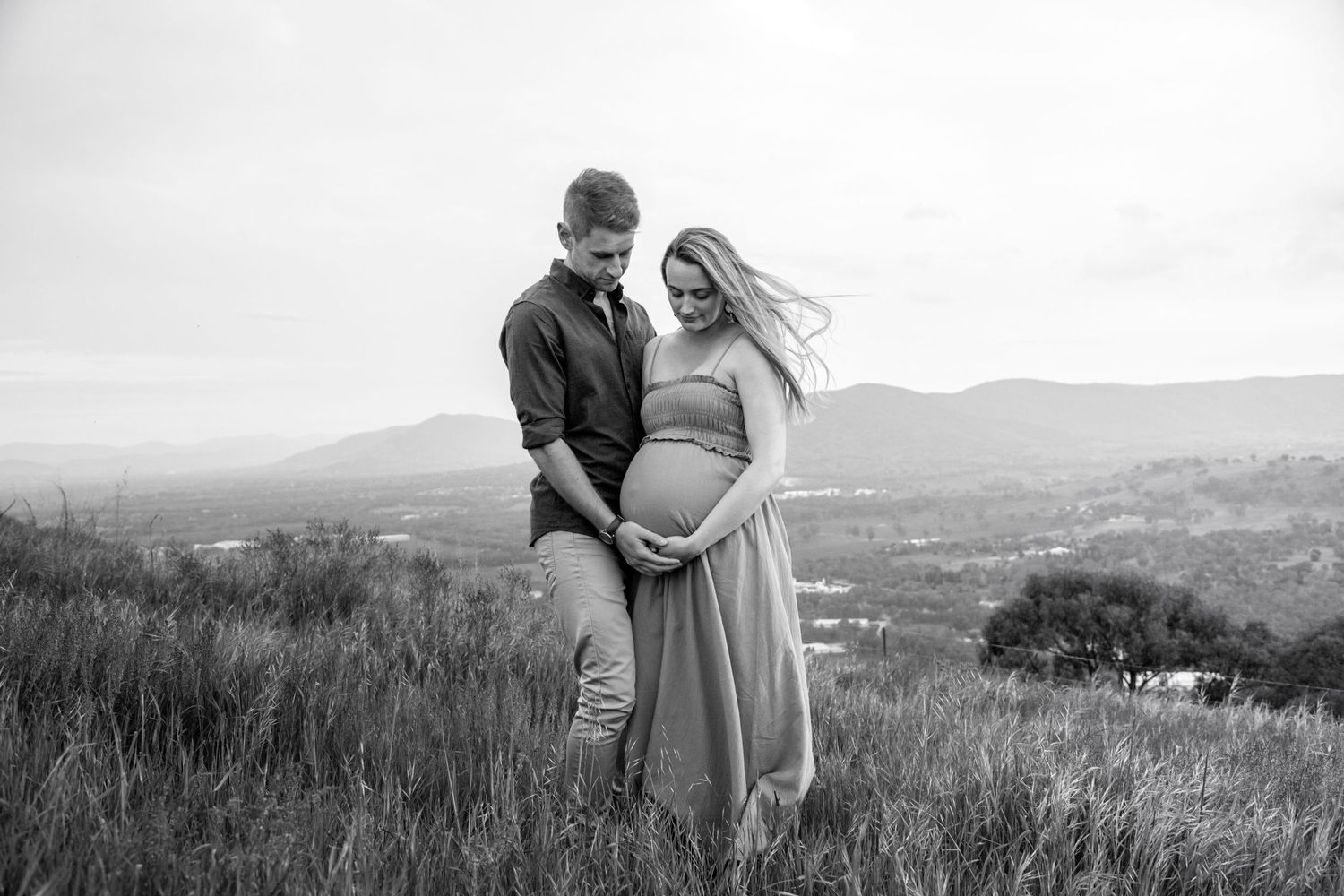 Black and white maternity photo of couple on hilltop with mountain vista in background.