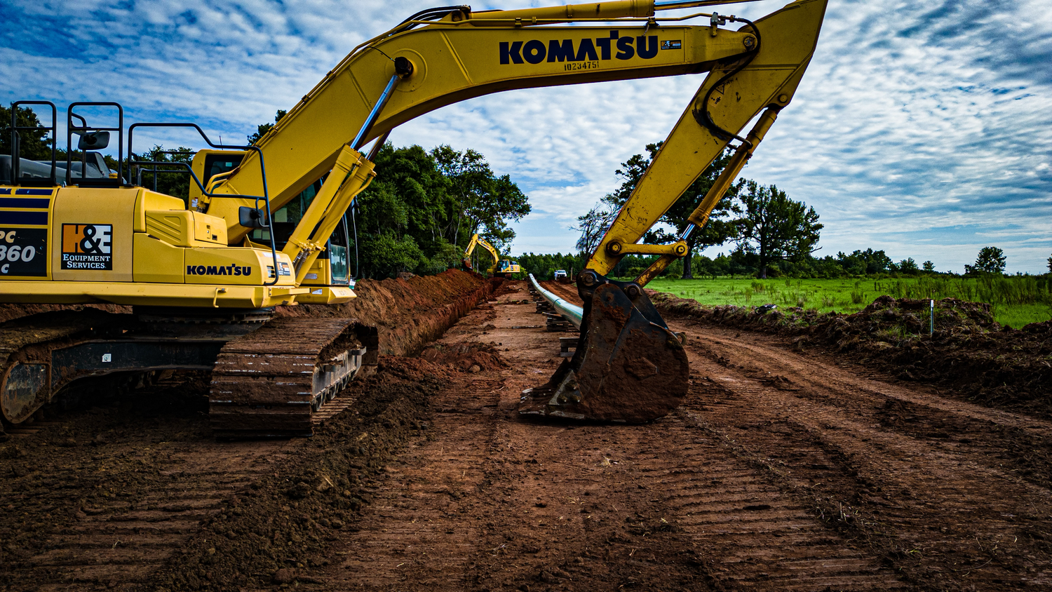 Yellow Komatsu excavator on dirt construction site against blue cloudy sky.