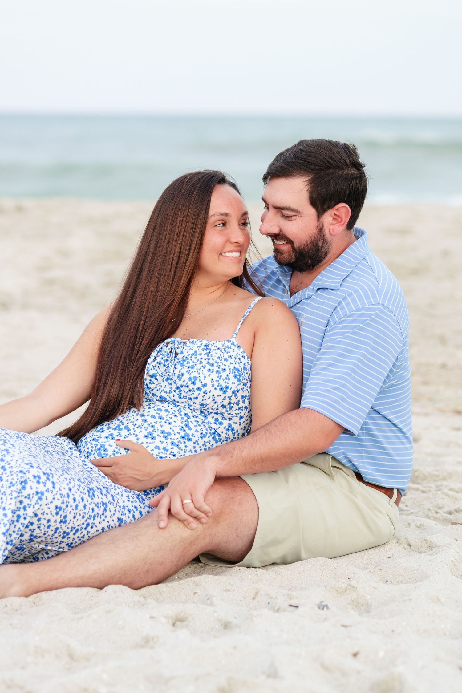 Intimate beach maternity photo showing couple in casual attire relaxing on sand.