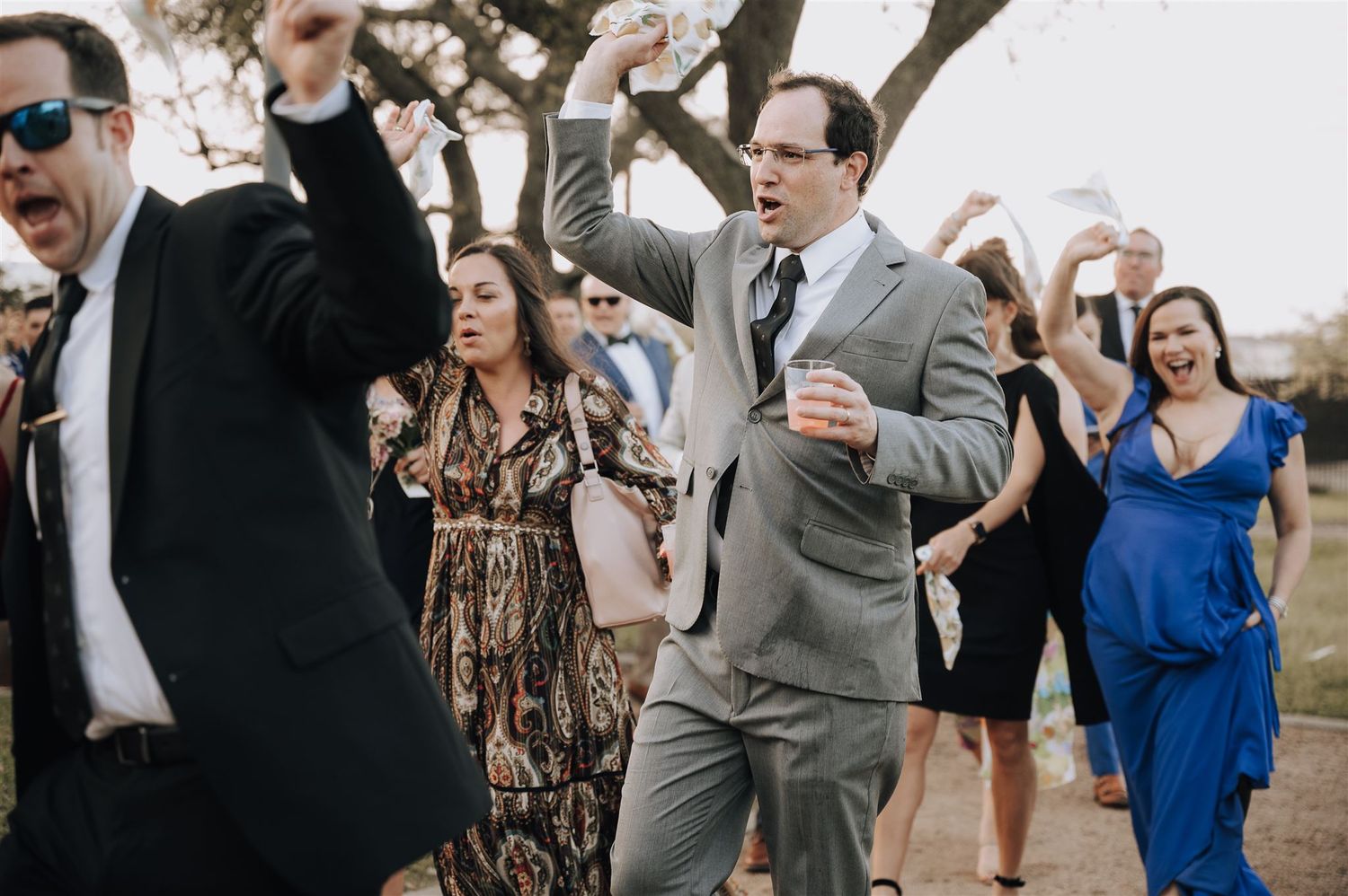 Wedding guests dance and celebrate outdoors during a reception.