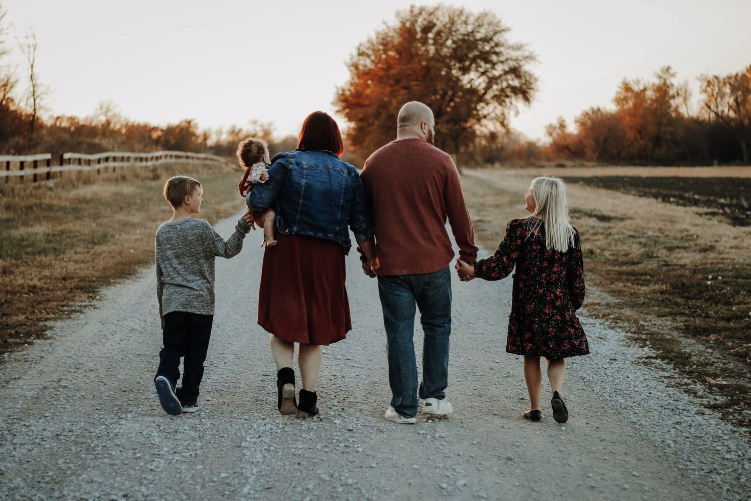 A family walks together along a path during sunset, captured from behind.