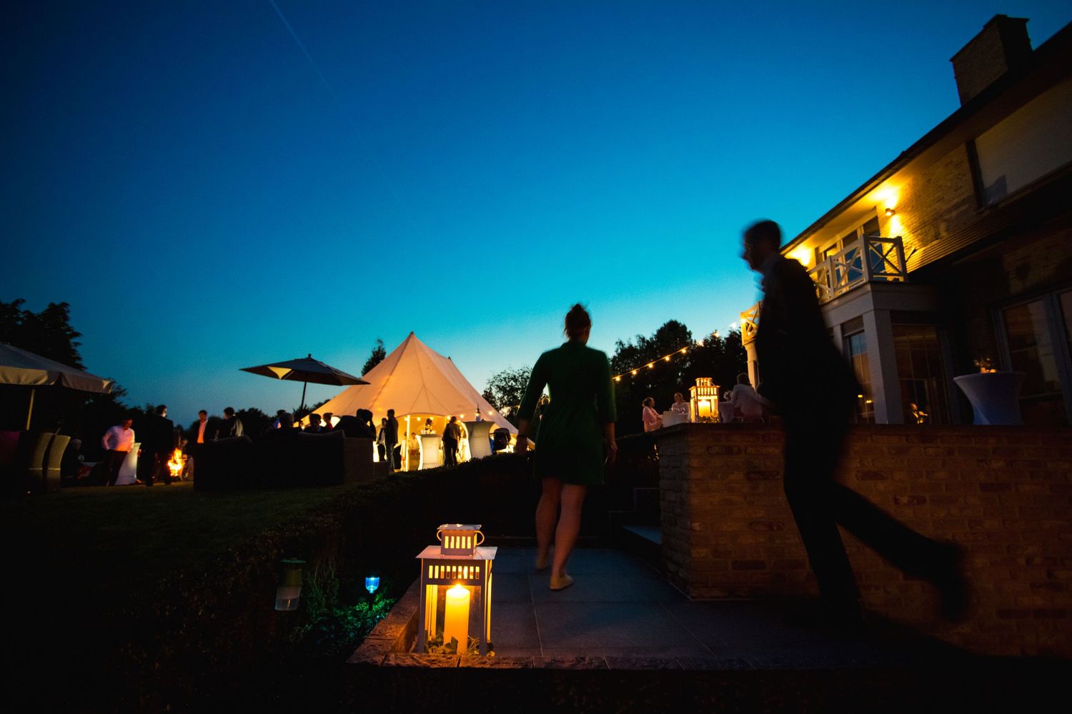 Evening wedding reception silhouettes against a blue twilight sky with lantern decorations.