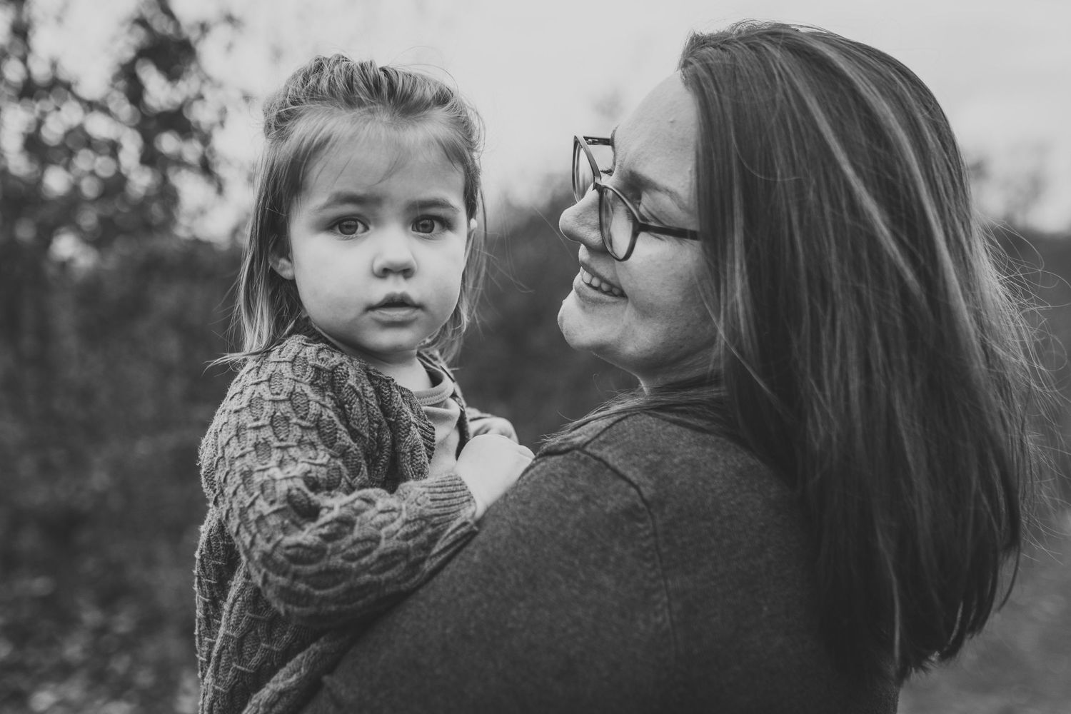 A touching black and white portrait showing a tender moment between parent and child embracing outdoors.