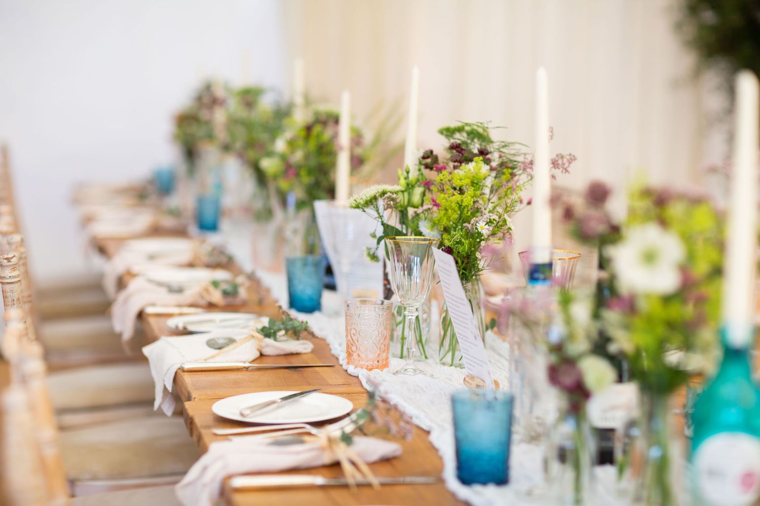 Elegant wedding table setting with blue glassware, natural greenery and soft floral centerpieces.