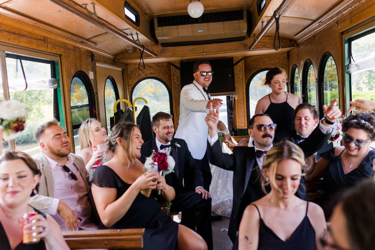 Wedding party celebrates with drinks inside vintage trolley during reception.