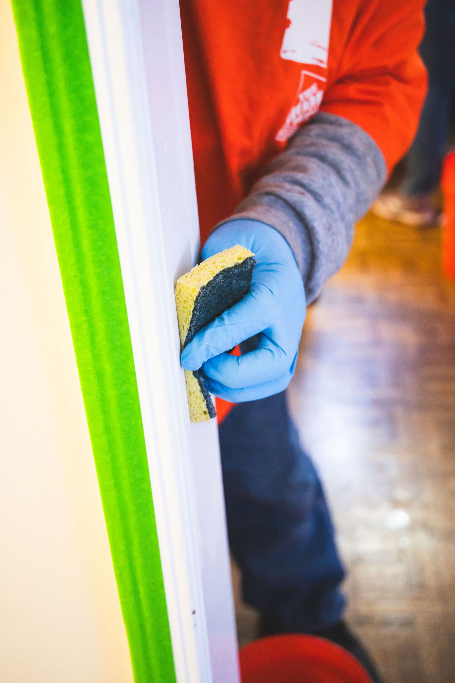 Hand wearing blue glove using sanding block on white trim work.