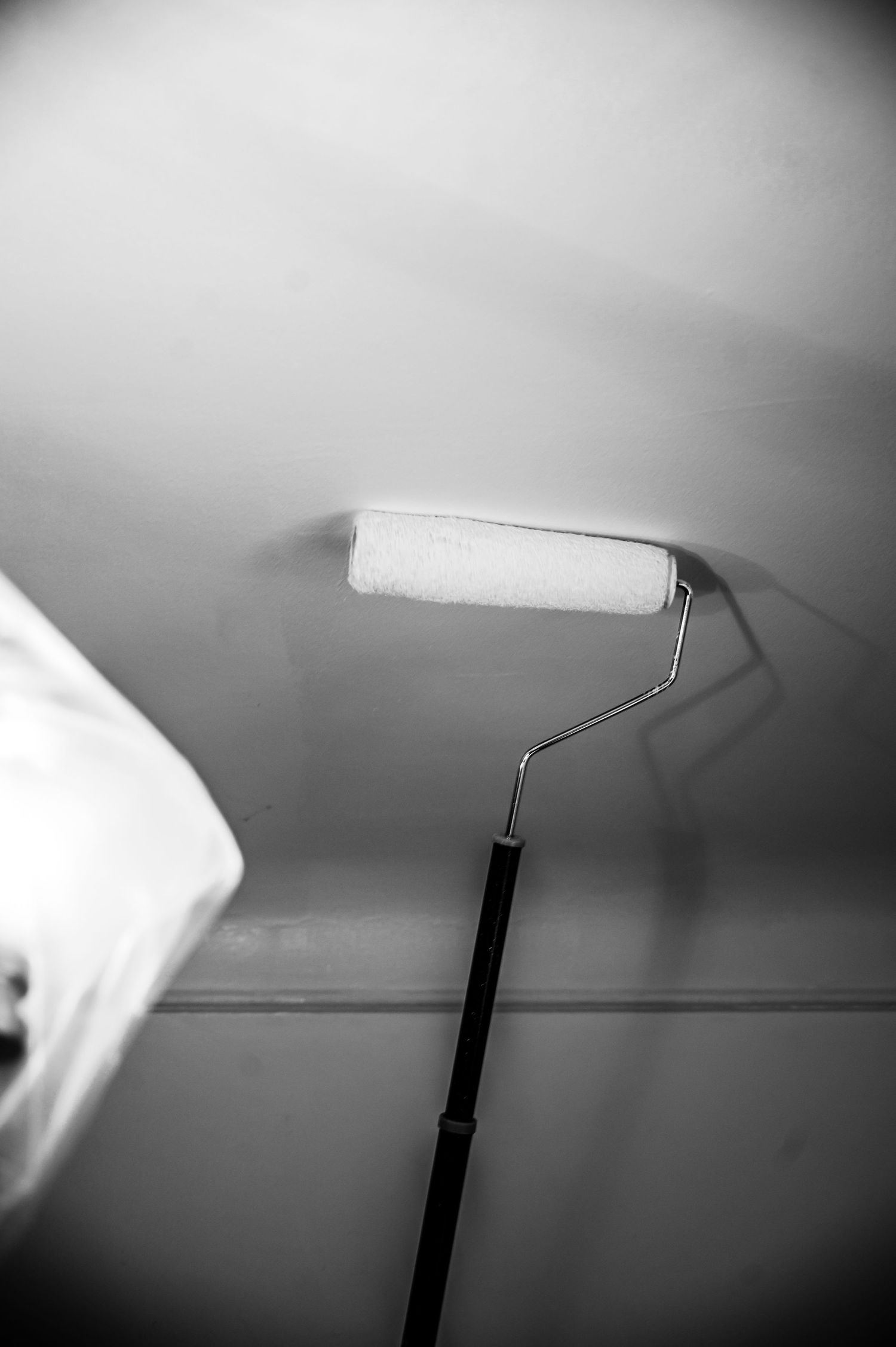 Paint roller extending to white ceiling in monochromatic composition.