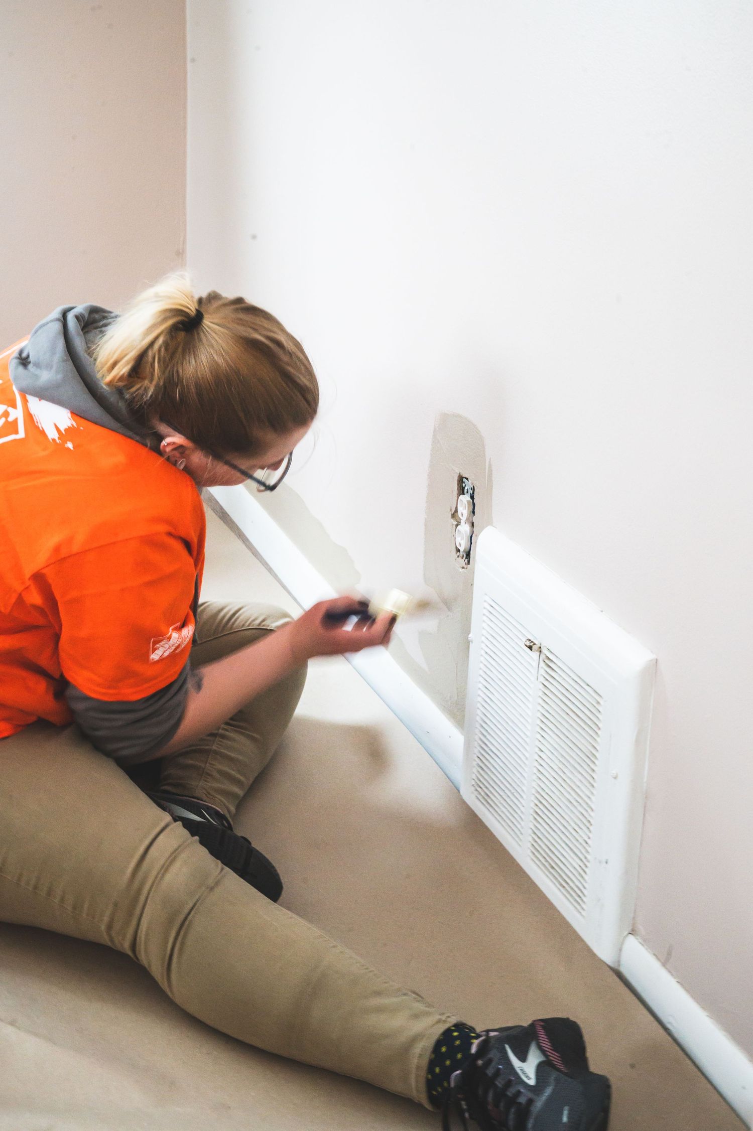 Someone in orange top examining an air vent cover during home maintenance.