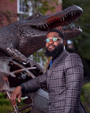 Creative graduation photo with plaid suit near alligator statue on campus.