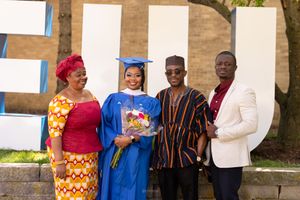A graduation celebration photo featuring a graduate in blue regalia surrounded by three others in colorful attire.