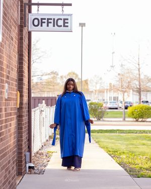Graduate wearing royal blue academic regalia walking outside office building on sidewalk.
