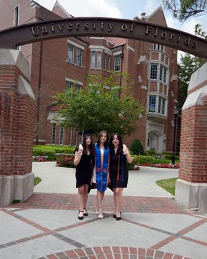 Three graduates pose in caps and gowns under the University of Florida entrance archway.