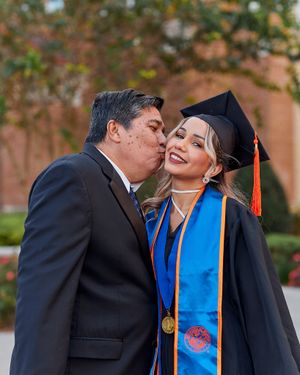 Emotional graduation moment with family member giving congratulatory kiss.