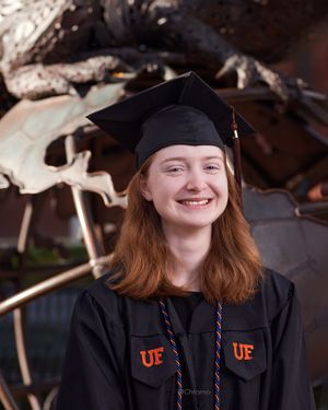 Graduate wearing black cap and gown with UF logo poses by campus building.
