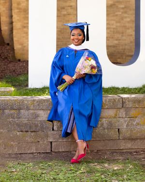 Graduate in blue cap and gown holds flower bouquet while posing on brick steps.