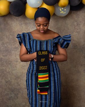 Graduate in striped dress with Class of 2022 text poses against balloon backdrop.