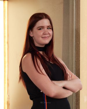 Professional portrait of someone in a black outfit standing confidently with arms crossed.