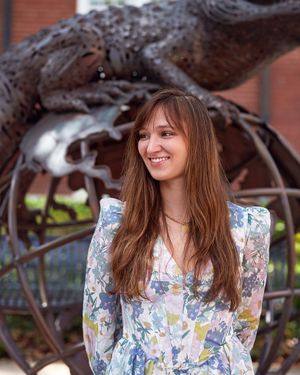 Portrait of someone in a floral dress standing by a unique metal sculpture.