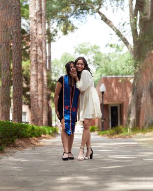Two graduates walking together on a tree-lined pathway at University of Florida.