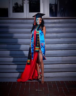 Graduate in blue and red regalia poses confidently on stone steps during graduation photoshoot.