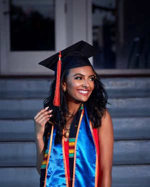 Graduation portrait featuring blue academic regalia and bright smile against classic architecture.