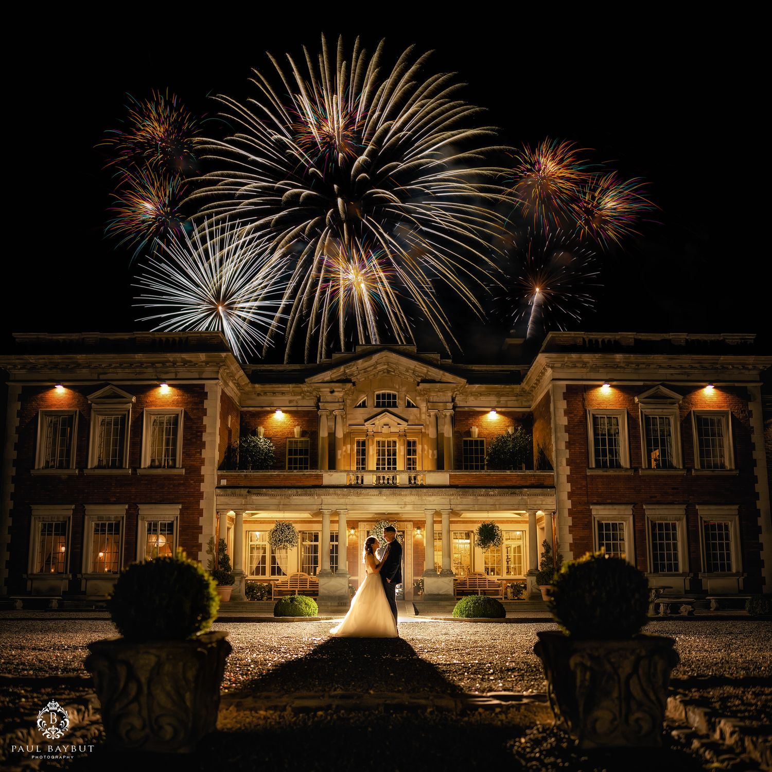 Spectacular fireworks illuminate the night sky above a grand historic mansion during a wedding celebration.