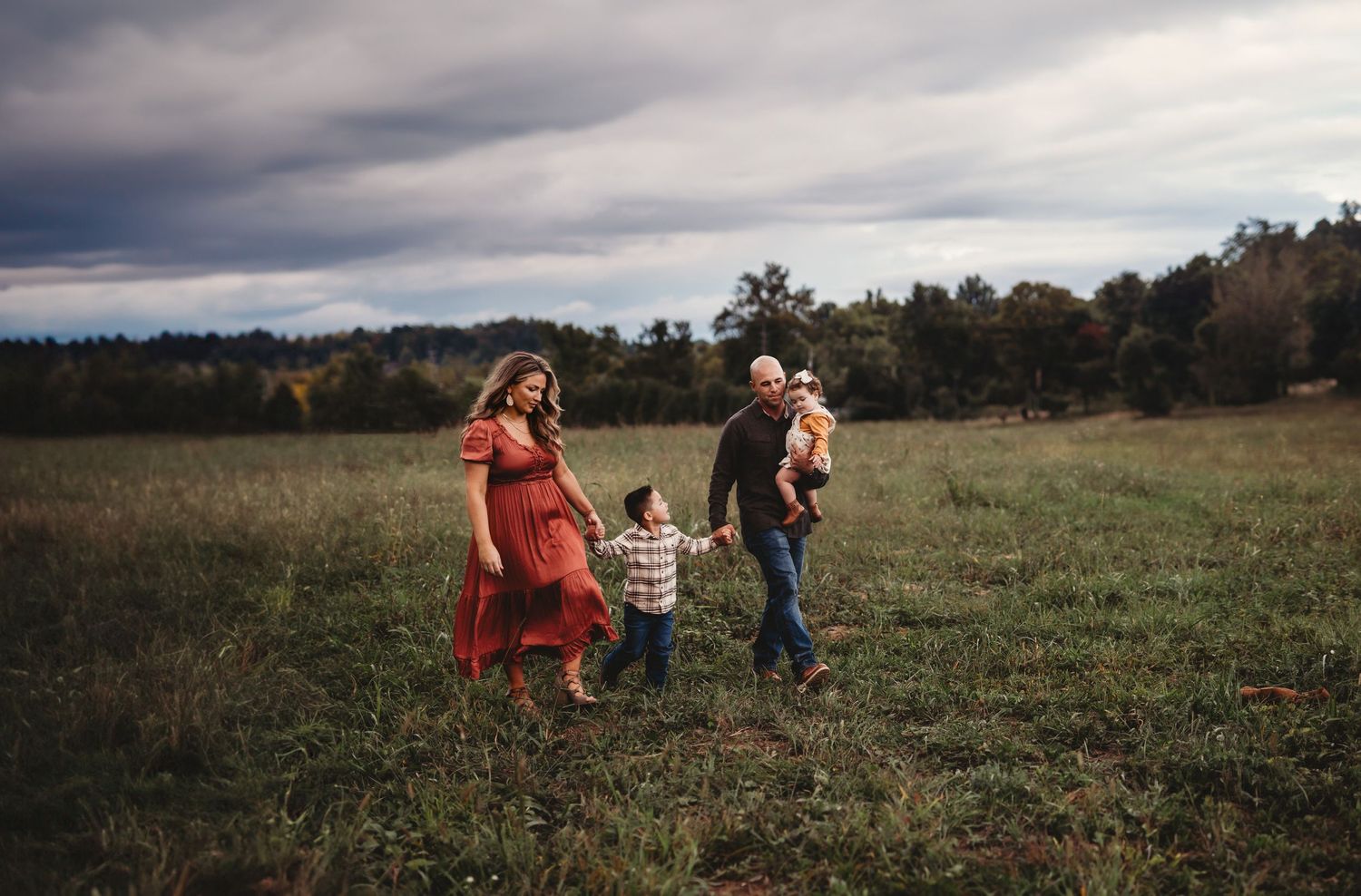 A family walks together through an open field under dramatic cloudy skies on an autumn afternoon.