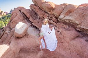 A white lace dress creates ethereal movement against dramatic red rock formations in natural light.