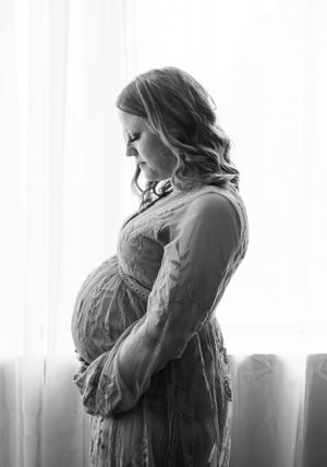 Black and white side profile of pregnant woman in lace dress by window.