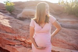 A pink maternity dress harmonizes with warm sunset light on red rock formations.
