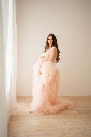 Maternity photoshoot featuring a flowing peach tulle gown in a minimalist setting with natural lighting.