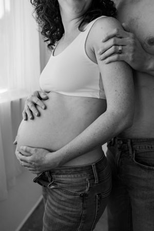 Black and white intimate maternity photo showing a couple embracing and cradling a pregnant belly.