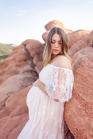 An off-shoulder white lace maternity gown creates elegant contrast against red rock formations.